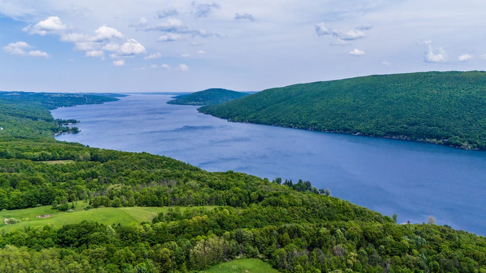 Wide aerial view of Canandaigua Lake running between densely wooded green hills.