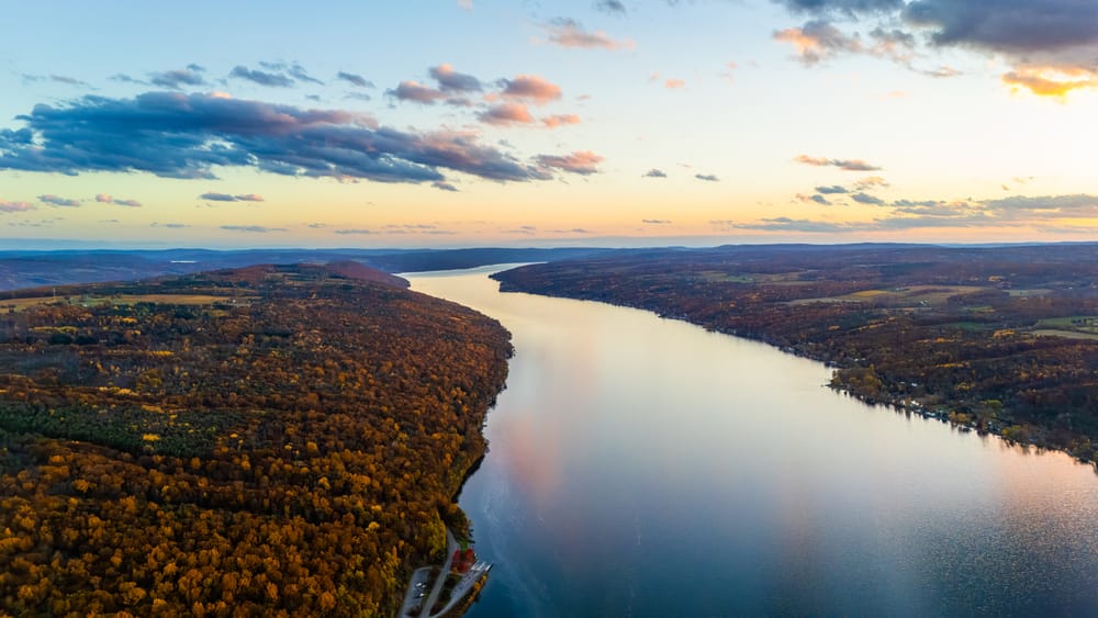 Aerial sunset view along a long Finger Lake bordered by forested hills in late autumn.