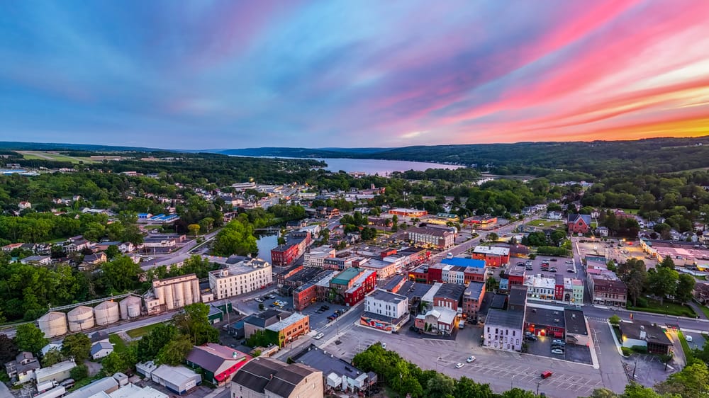 Aerial twilight view of downtown Penn Yan with colorful sunset clouds and Keuka Lake in the distance.
