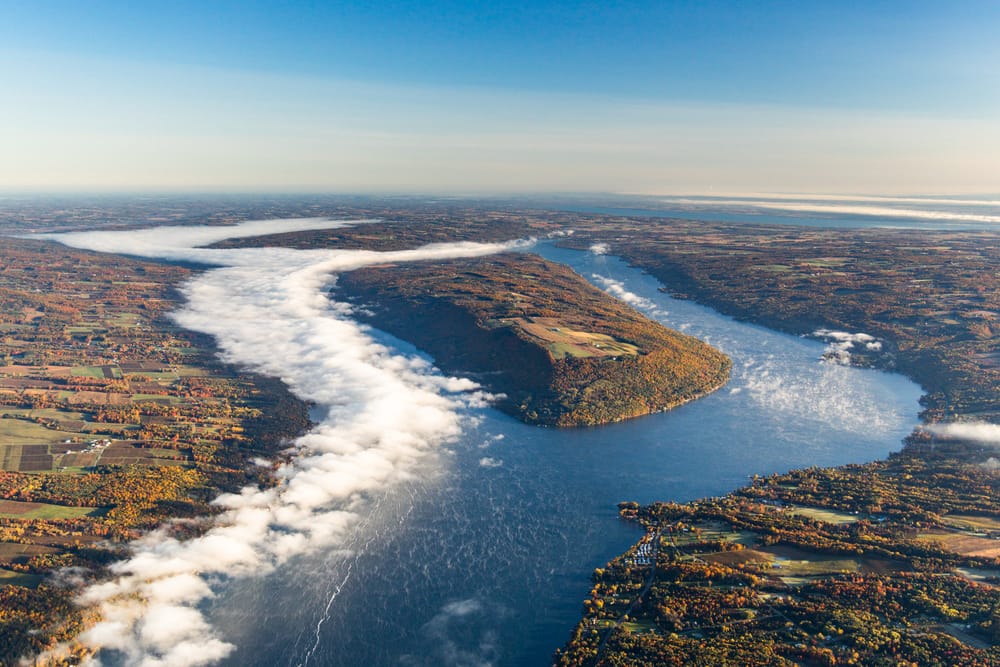 Very high aerial view of Keuka Lake's branching shape with bands of white fog and autumn farmland.